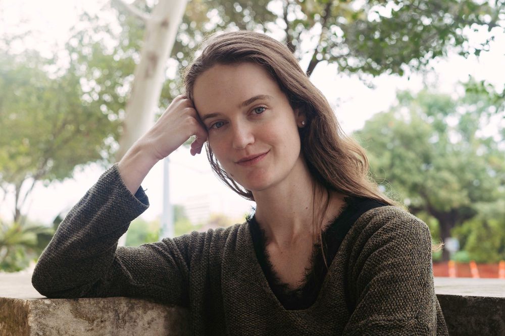 Casual portrait of person in dark sweater resting head on hand outdoors.