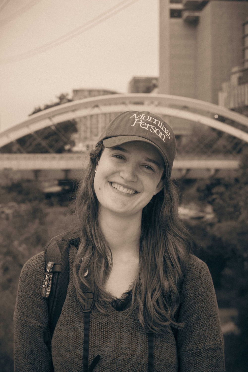 Sepia portrait of person wearing Morning Person baseball cap and  sweater outdoors.