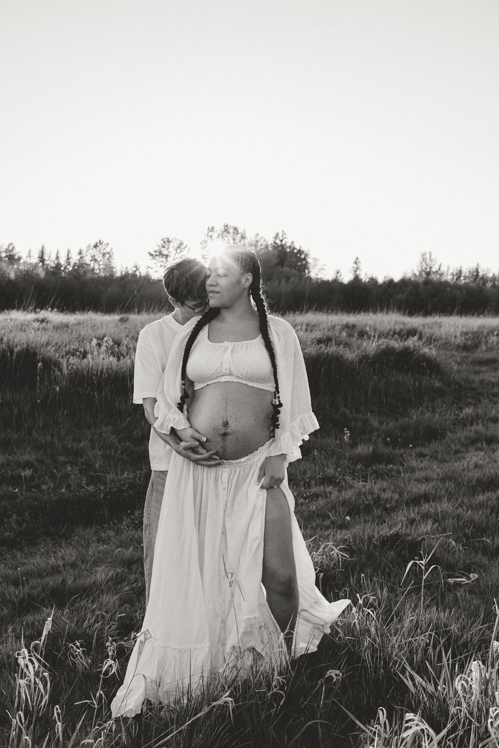 A black and white photo of someone in a flowy white dress standing in a grassy field at sunset.