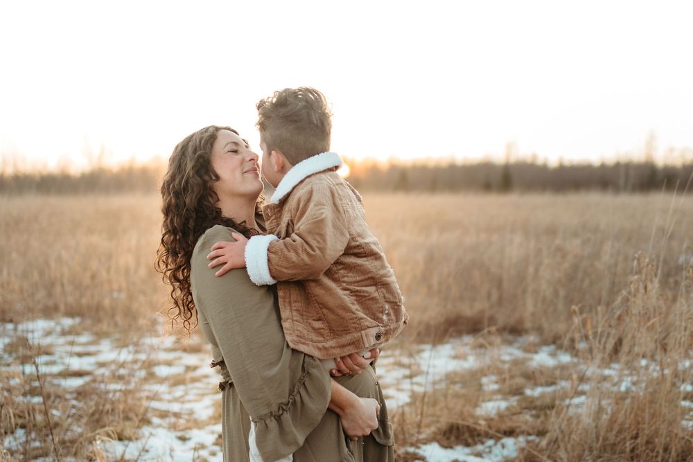 A loving embrace shared between parent and child in a winter field at sunset with tall grass in the background.