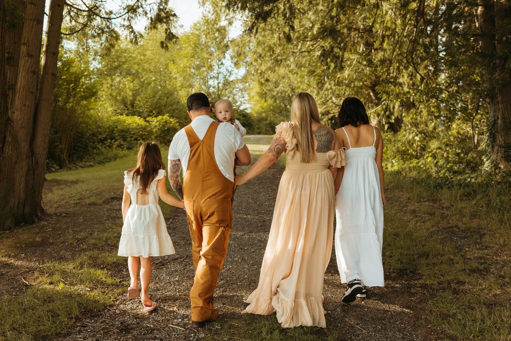 Family wearing coordinated neutral outfits walks together through a sunlit forest path during golden hour.