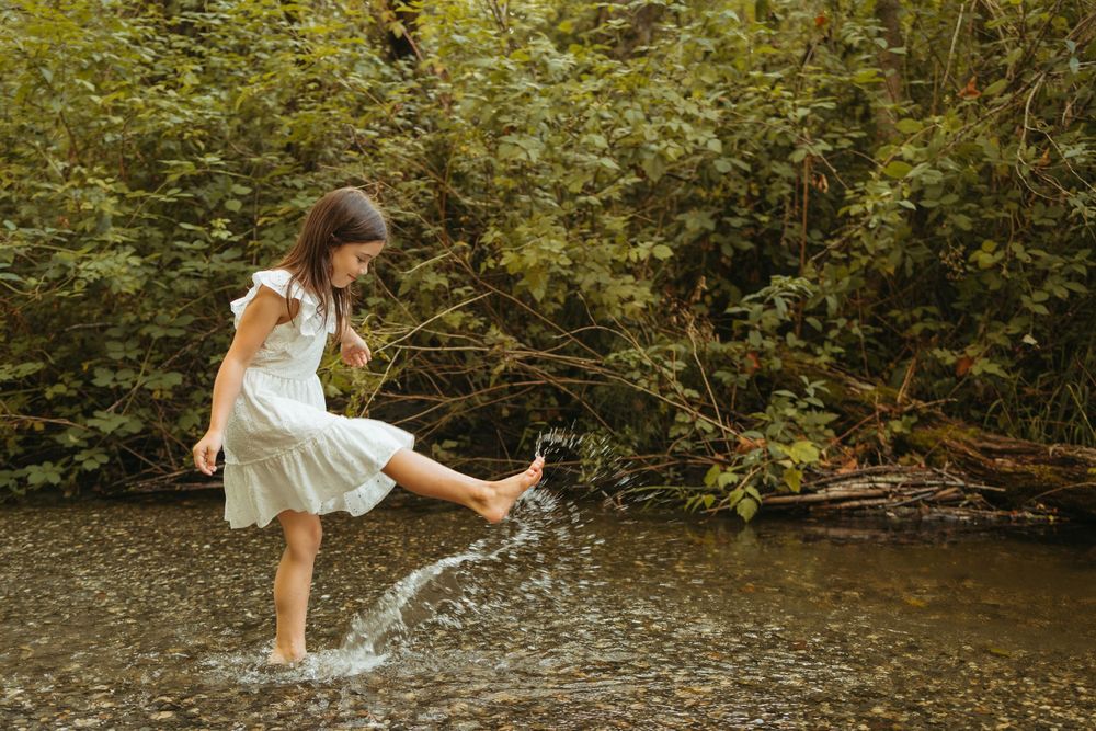 A person in a white dress dances gracefully in a forest stream, creating a serene and ethereal scene.