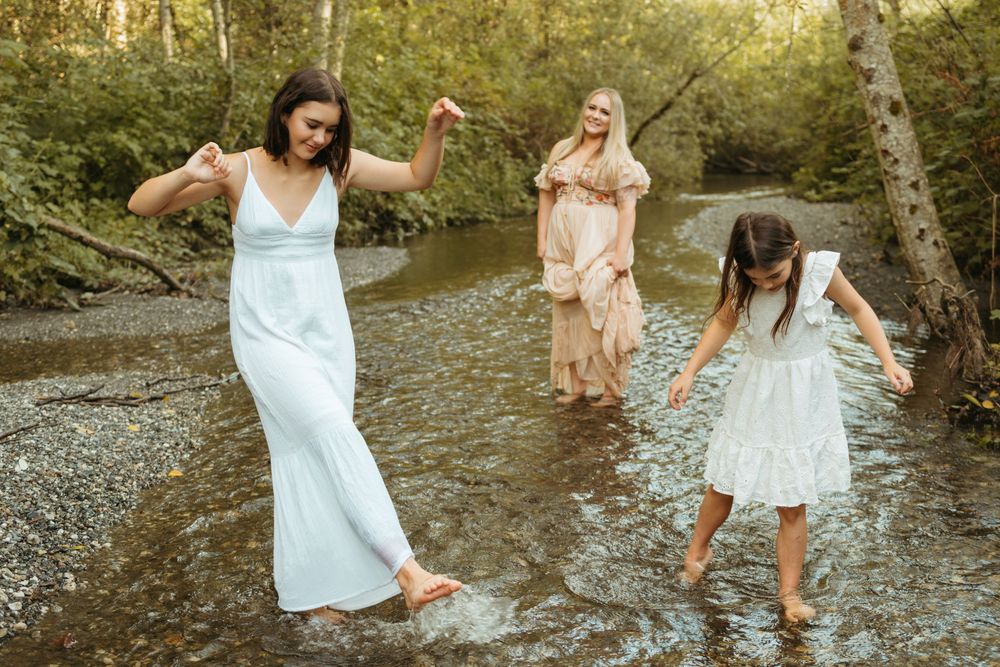 Group in light flowy dresses splash and play together in a sunlit creek on a warm summer afternoon.