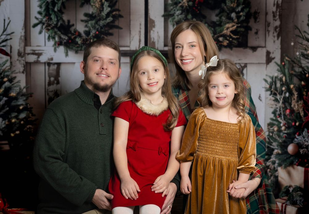 A festive holiday portrait featuring a family of four in front of a decorated doorway with wreaths.