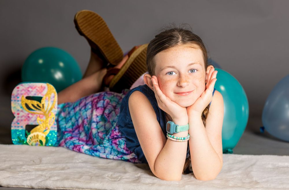 Child in mermaid dress lying on floor with birthday party decorations.
