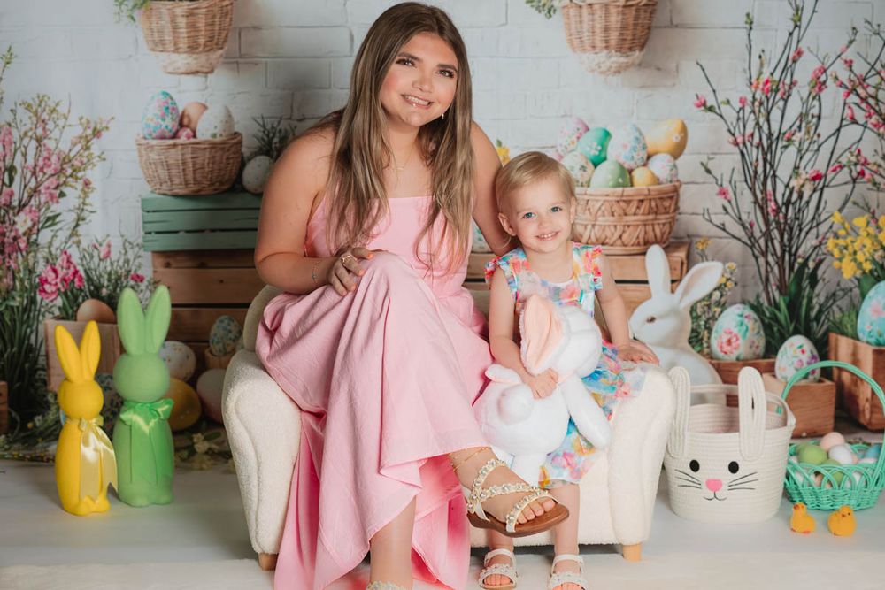 Springtime portrait featuring pink and white dresses against an Easter-themed backdrop with colorful bunnies and floral decor.