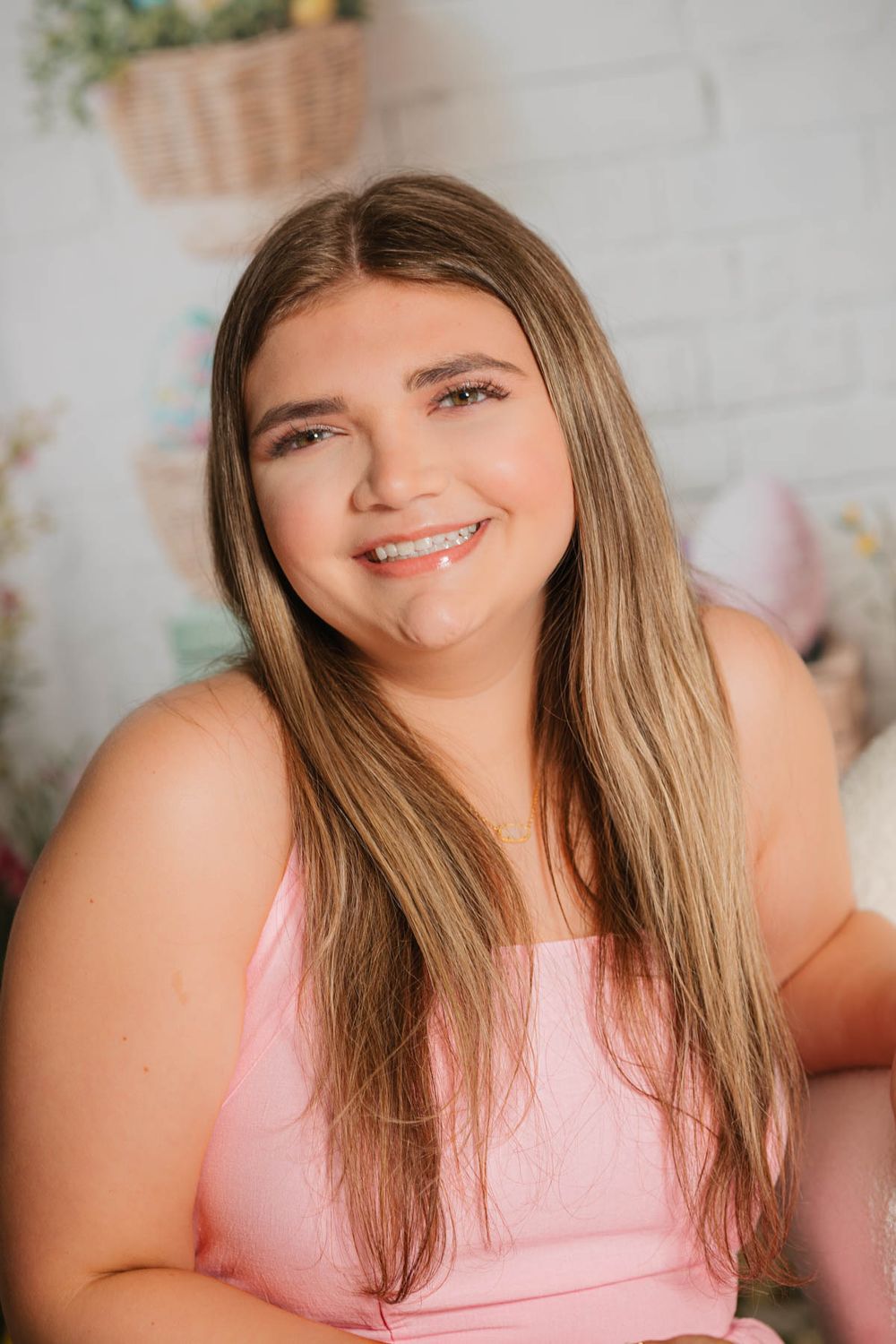 A bright portrait of someone wearing a pink top and long blonde hair smiling warmly against a light-colored background.