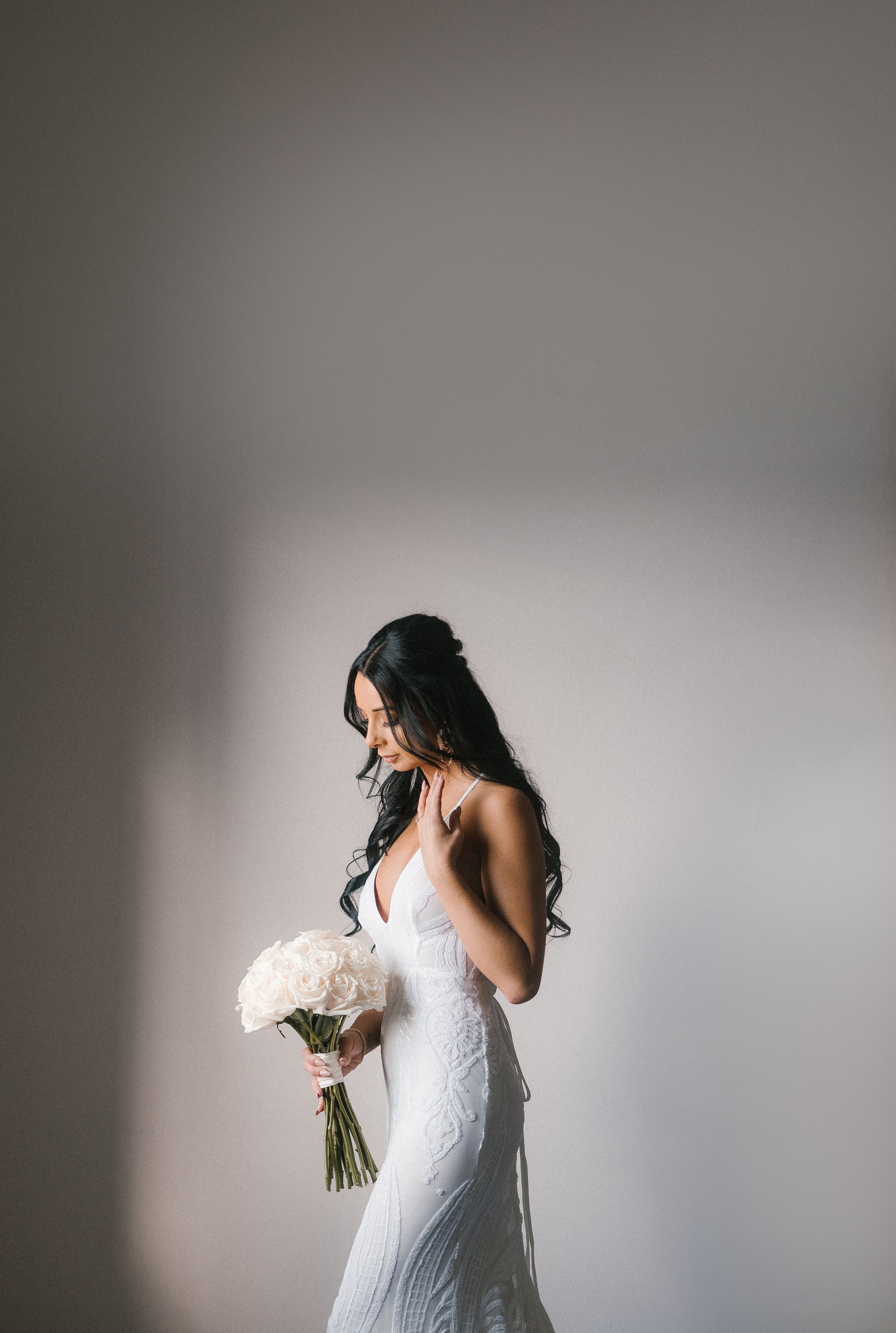 Artistic side profile of a bride in white dress holding a bouquet against neutral background.