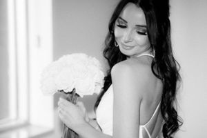 Black and white photo of bride with long dark hair holding white bouquet.
