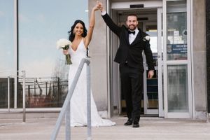 Newlyweds exit building with joyful celebration and raised arms.