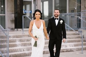 Elegant couple in wedding attire walking down stone steps.