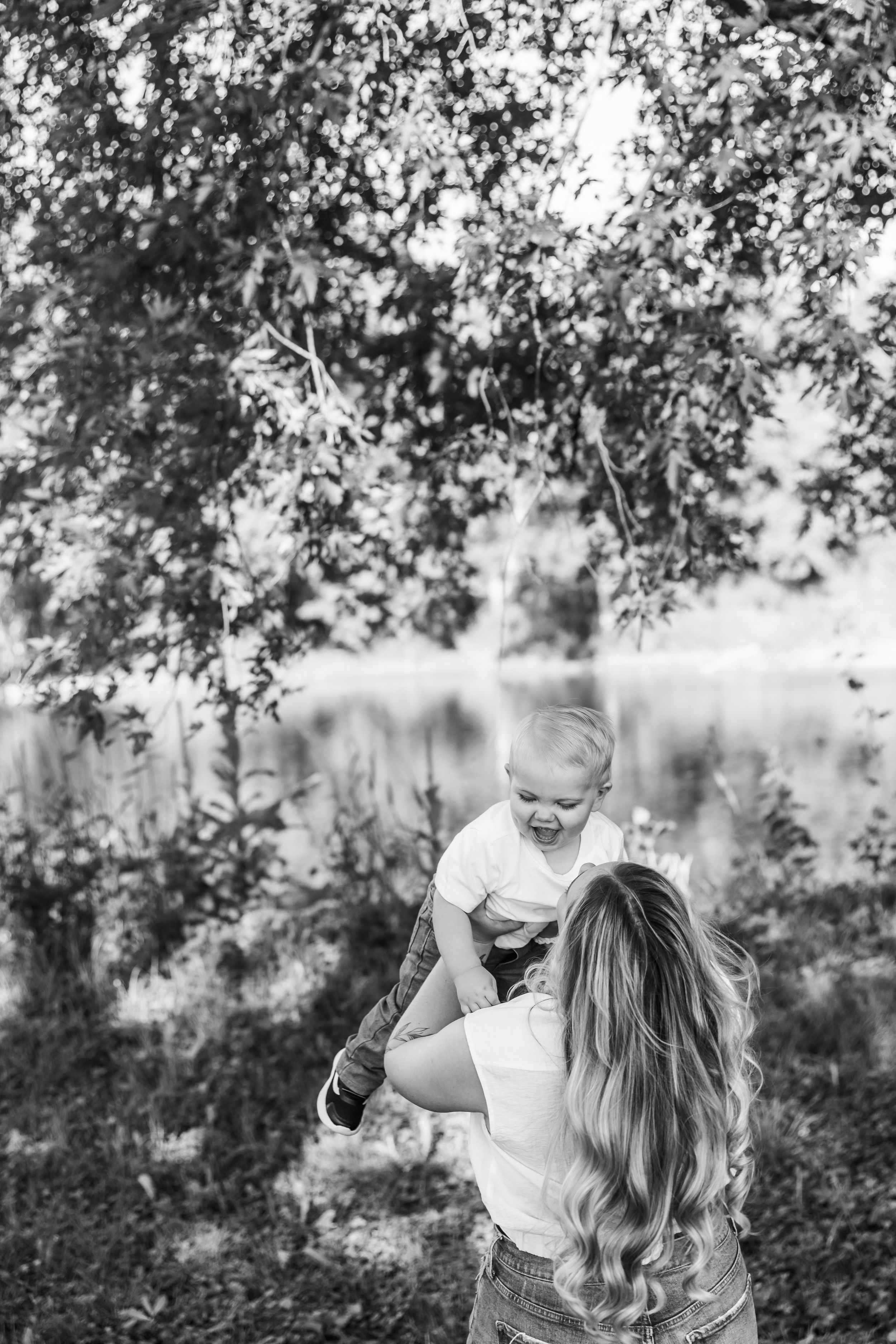 A tender family moment captured under tree branches in black and white.