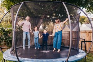 People jumping and playing on a large backyard trampoline.