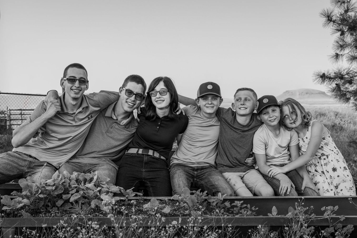 black and white image of a young kid is sitting on the shoulders of a guy with elbow resting on the head of the girl next to him