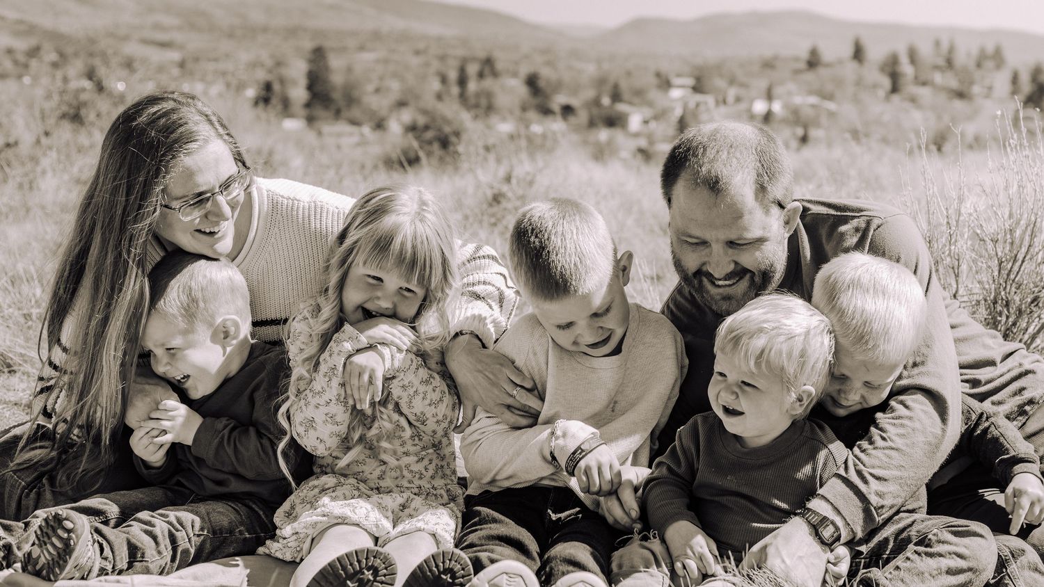 black and white image of a young kid is sitting on the shoulders of a guy with elbow resting on the head of the girl next to him