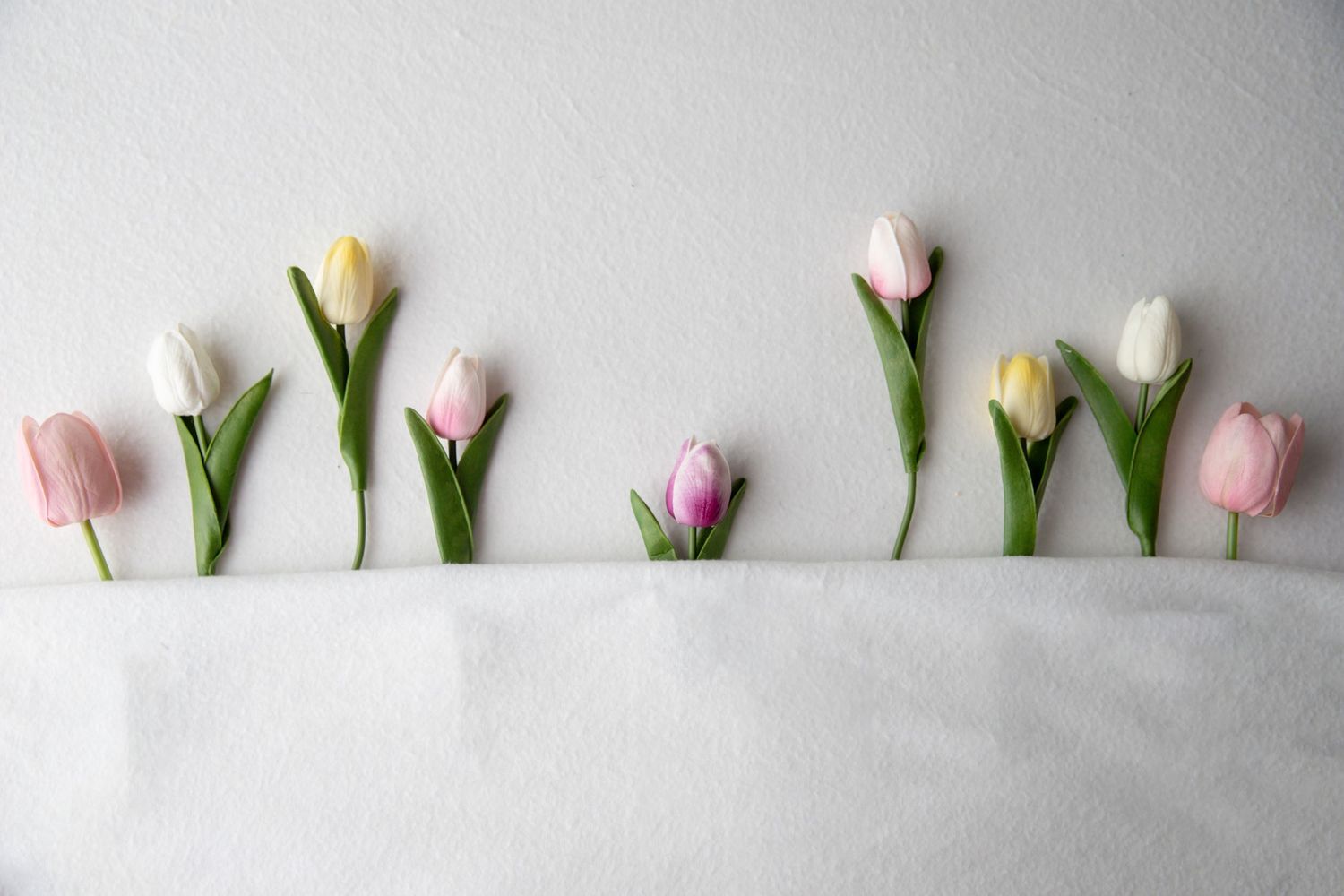 Row of pastel pink, yellow, white, and purple tulips arranged on a white surface.