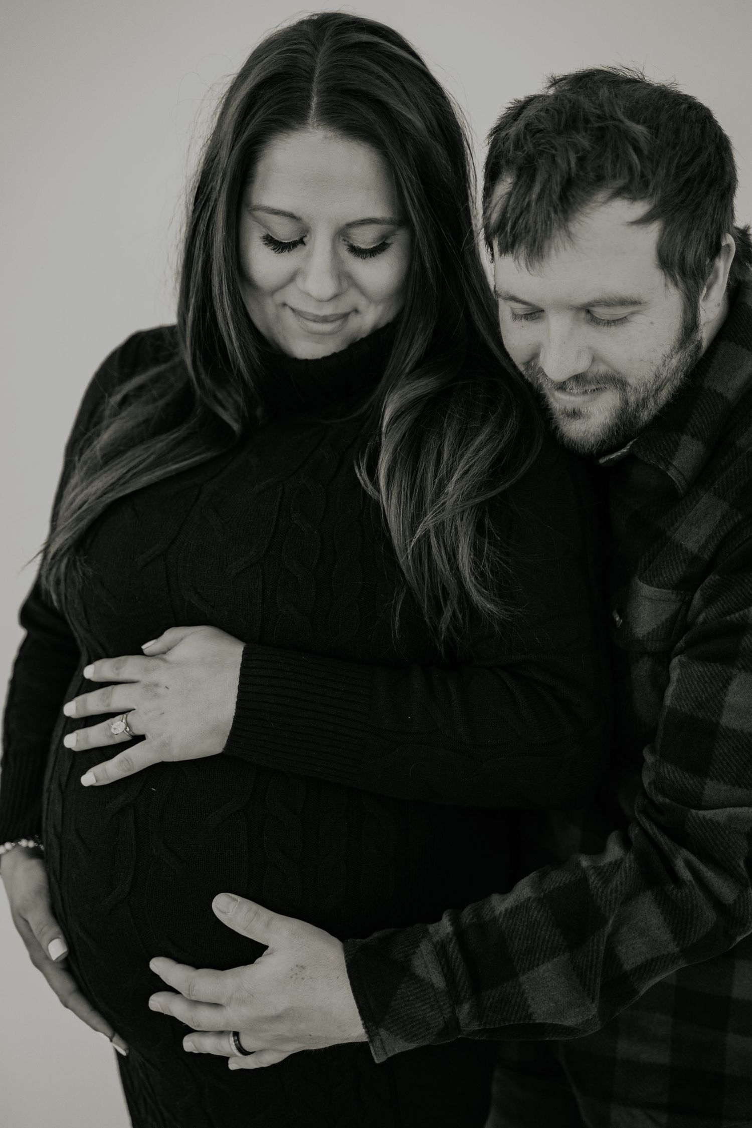 A black and white maternity photo showing couple gently touching the pregnant belly in an intimate moment.