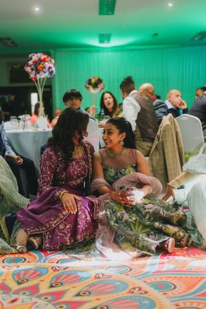 Wedding guests enjoying conversation at a reception with green lighting and colorful decor.