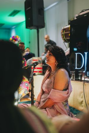 A performer sings at a wedding reception with DJ equipment visible in the background.