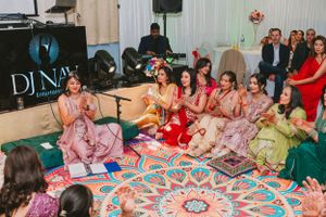 Group of attendees in pink traditional outfits seated on floor cushions at a cultural celebration.