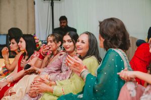 Guests in vibrant traditional attire clapping and enjoying festivities at an indoor celebration.