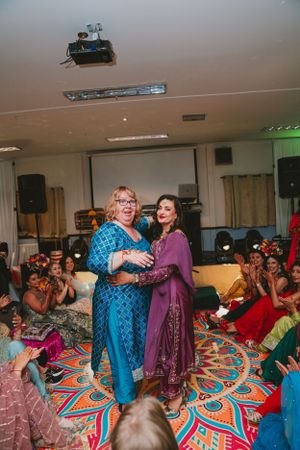 Two performers in blue and purple outfits entertain guests seated on a colorful patterned carpet.