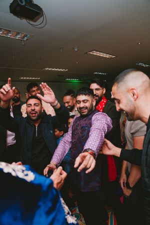 Group of men dancing and celebrating during indoor cultural event with green accent lighting.