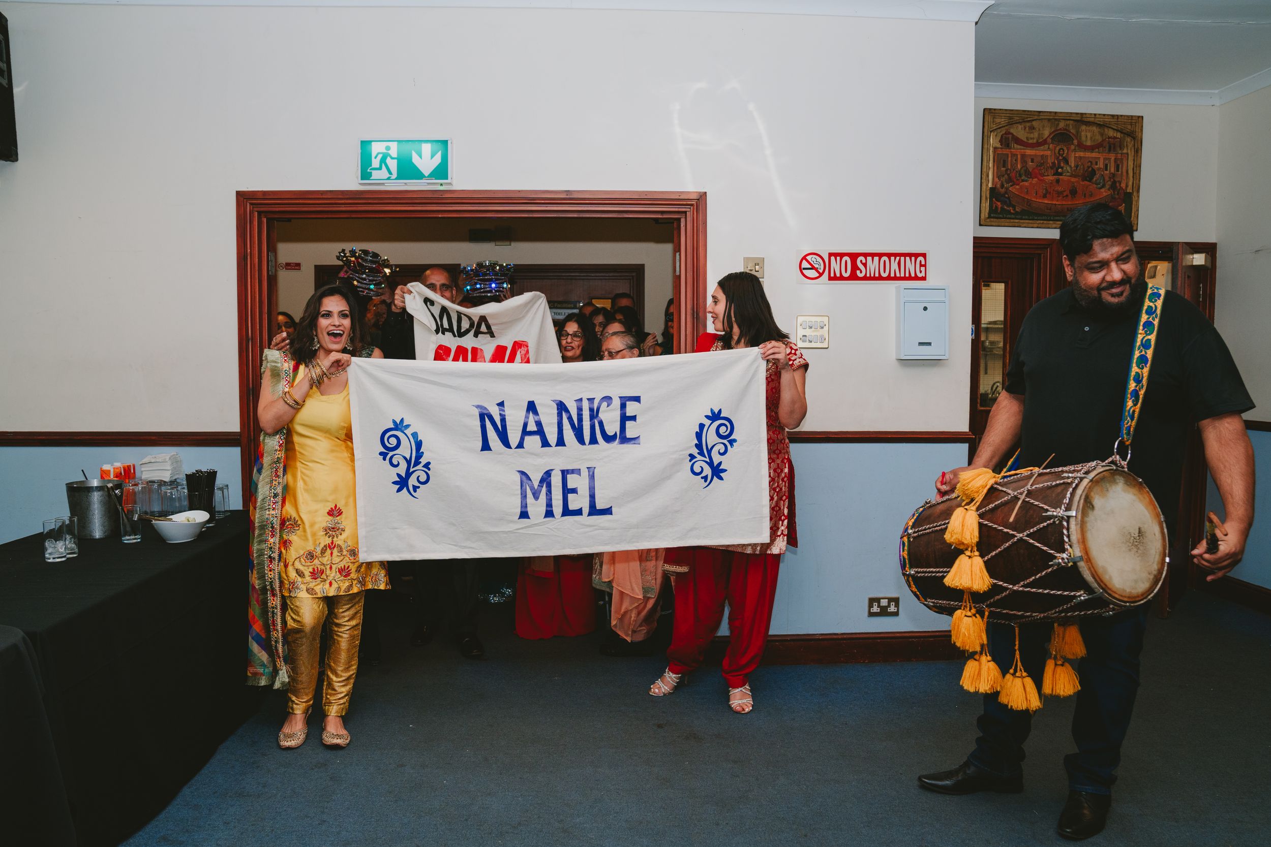 People holding a banner at a cultural celebration with drummers in traditional dress.