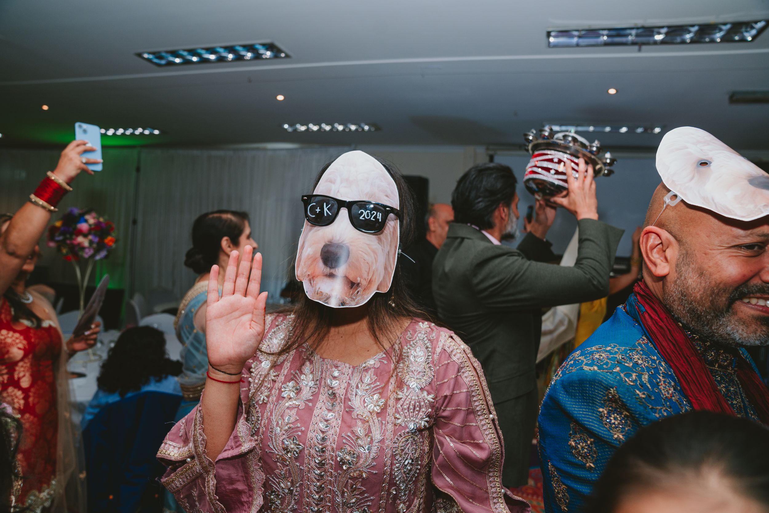 A celebratory gathering with people dancing and one person wearing a novelty face mask.