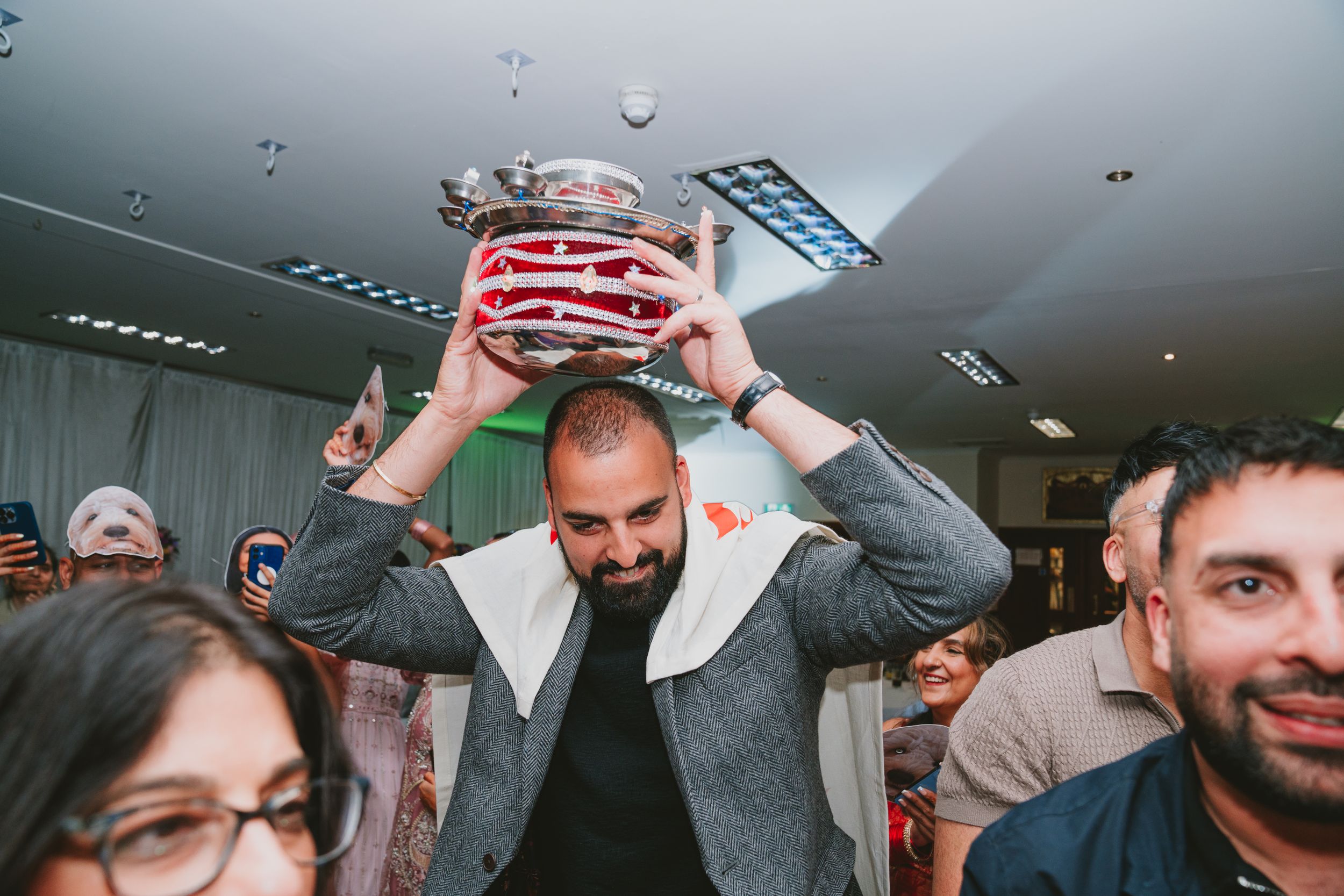 Guest lifts a decorated metal pot overhead during a festive celebration.