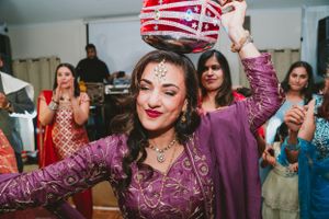 Guest in purple attire performs traditional dance while balancing decorated pot.