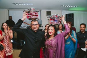 Couple in formal attire lifting matching crowns during a festive celebration.