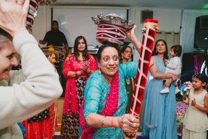 Guests in colorful traditional attire dance and celebrate while holding ornate ceremonial poles.