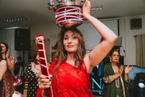 Guest in red attire balances decorated pot during indoor celebration.