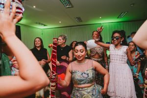 Celebration in a room with green lighting as party guests dance with decorative poles.