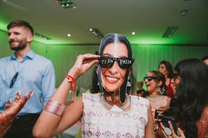 Party guest wearing sunglasses smiles during celebration with green ambient lighting.