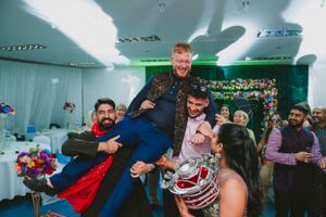 Partygoers lift and carry someone during a lively indoor celebration.