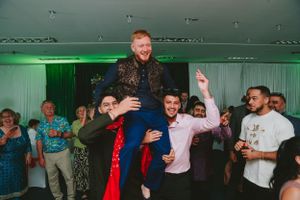 Celebrants lift someone up during a festive indoor party with green accent lighting.