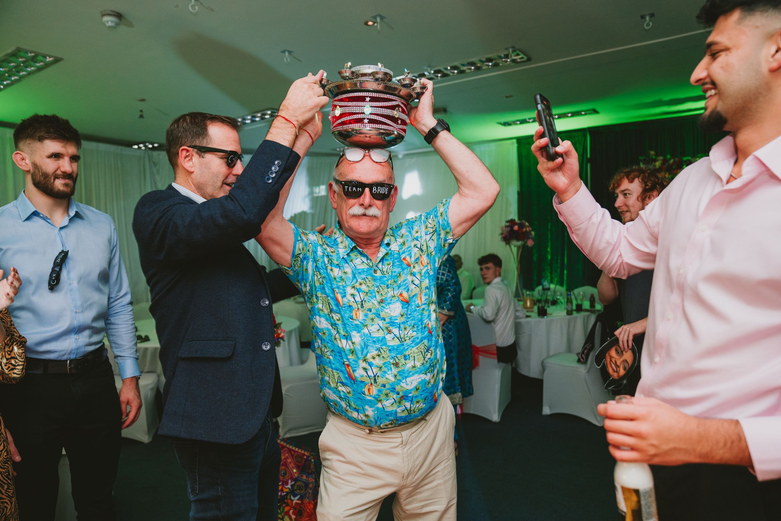 Party guests place a crown on someone's head during a celebration with green lighting.