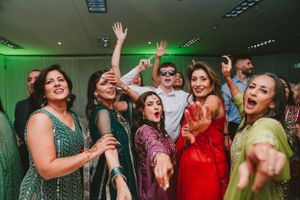 A group of party guests dance enthusiastically together wearing colorful formal attire.