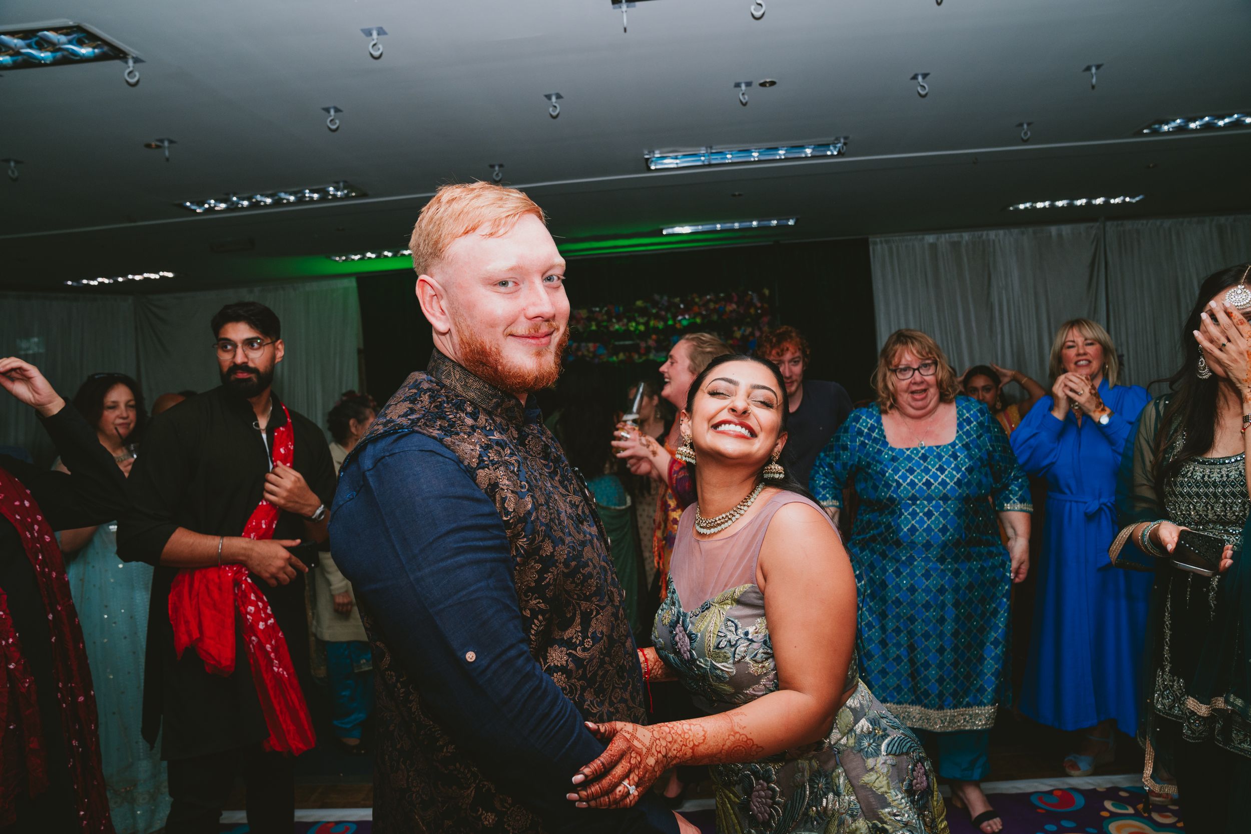 Guests dance together at a celebration with colorful formal attire and ambient lighting.