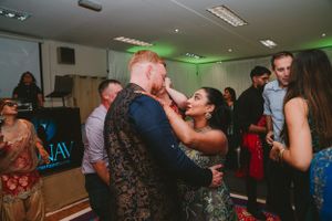 Couples dance together at an indoor celebration with ambient green lighting.