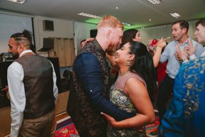 Couples dance closely during a festive indoor celebration with green accent lighting.