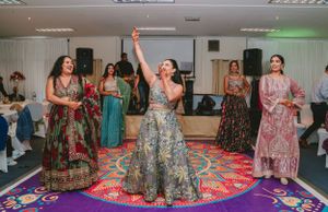 Festive group dancing together at a celebration on a vibrant patterned carpet in a decorated indoor venue.