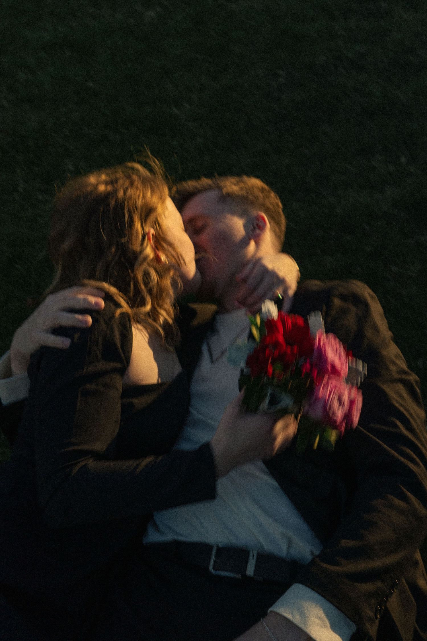 Romantic couple sharing an intimate moment while holding vibrant red flowers at sunset.