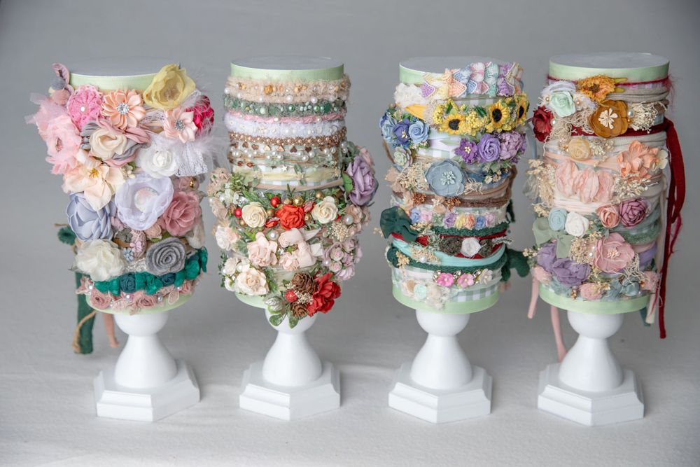 Four white pedestals showcasing elaborate floral and embellished headbands in pastel spring colors.