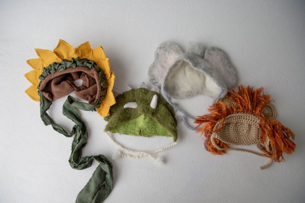 Four novelty baby hats including a sunflower, green leaf, gray bunny, and lion character designs.