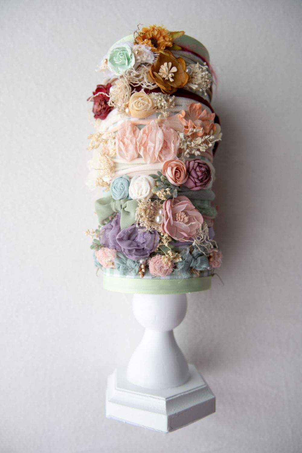 Assortment of pastel floral baby headbands stacked on white pedestal stand.