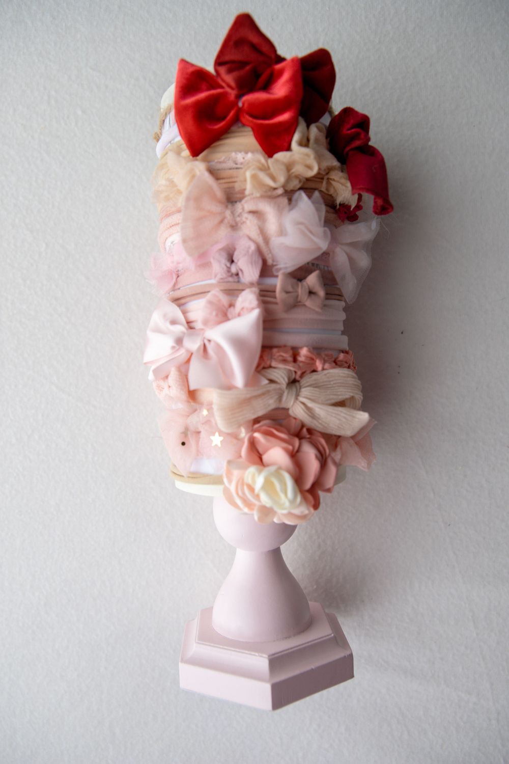 Pink pedestal displaying stacked red and pink satin hair bows and headbands for baby girls.