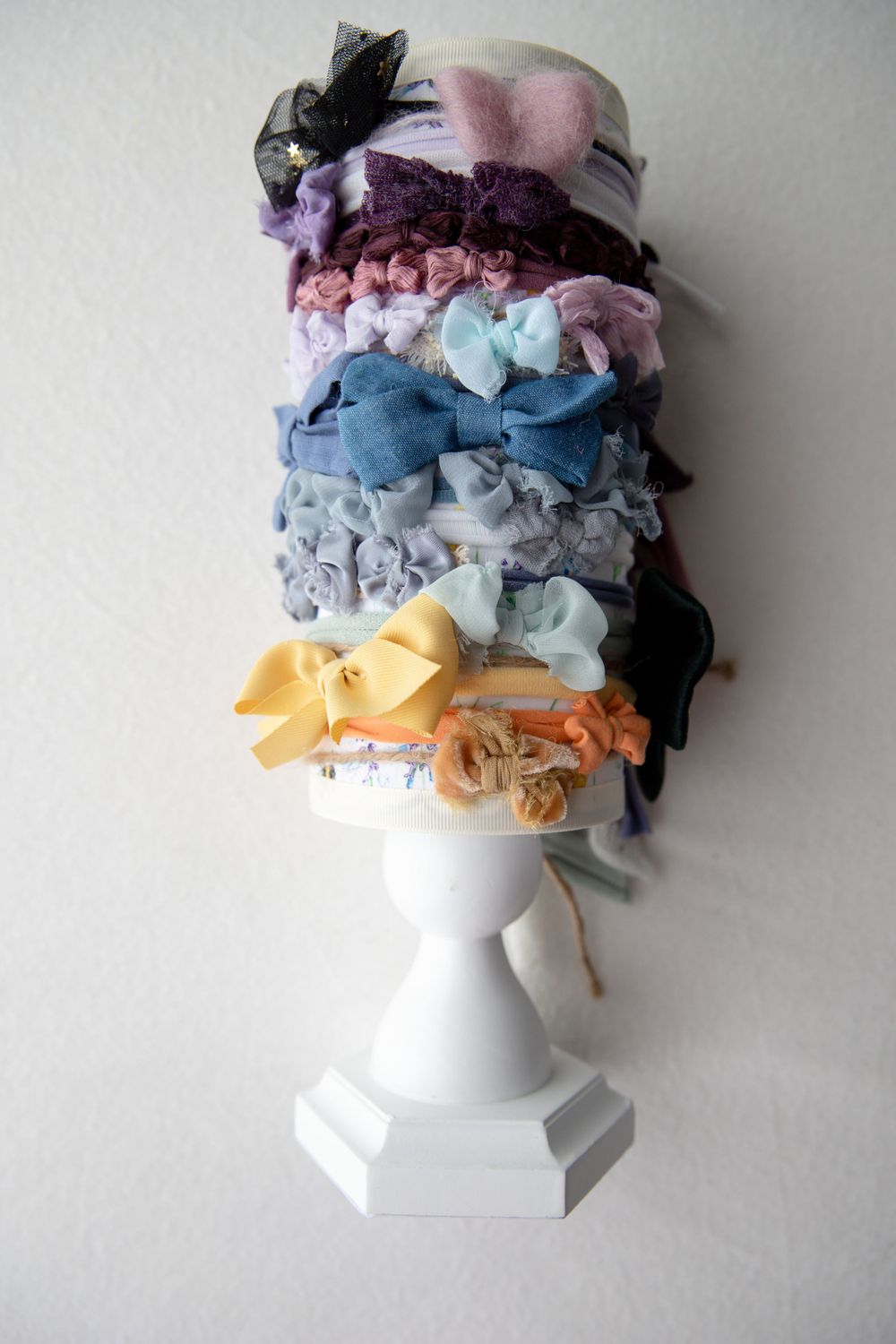White pedestal showcasing stacked colorful fabric hair bows and headbands in pastel tones.